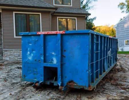 A blue dumpster parked in front of a house, providing a convenient waste disposal solution.